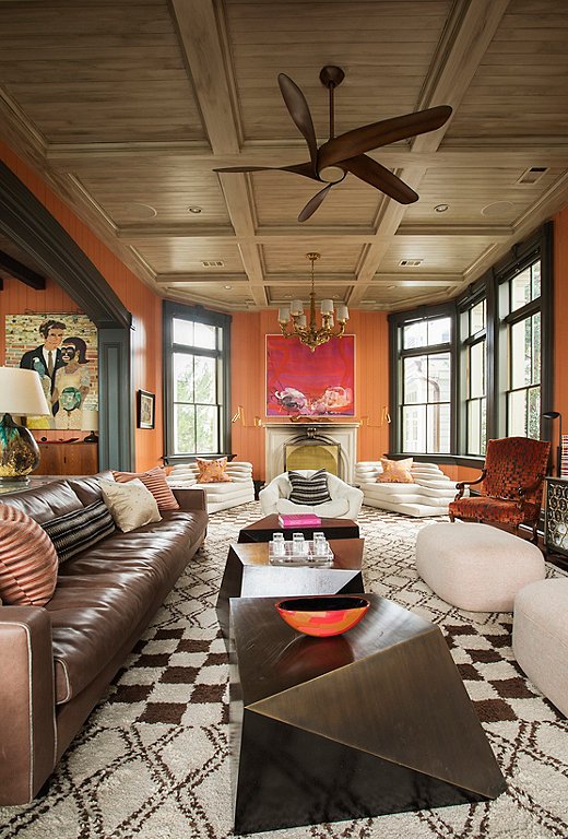 Warm, welcoming, and just a tad irreverent, the family room exudes a fun ’70s vibe with its terracotta walls, plush leather sofa, and poufs. A trio of Jean de Merry side tables and a contemporary ceiling fan bring sculptural energy to the room. Works by Savannah artists Betsy Cain (above the fireplace) and Marcus Kenney (left) offer modern, local color.  
